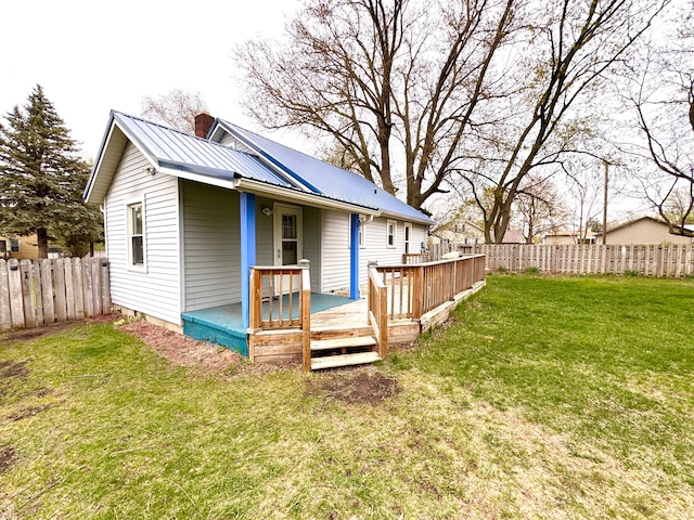 back of house featuring a fenced backyard, a yard, a chimney, and metal roof