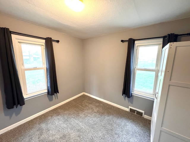 carpeted empty room featuring a textured ceiling, visible vents, and baseboards