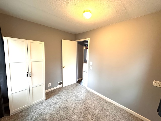 unfurnished bedroom with carpet flooring, a textured ceiling, and baseboards