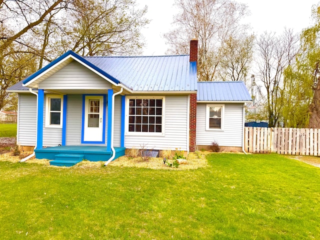 rear view of property featuring fence, covered porch, a chimney, metal roof, and a yard