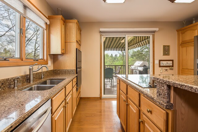 kitchen featuring a sink, light wood-style flooring, wall oven, stone counters, and stainless steel dishwasher