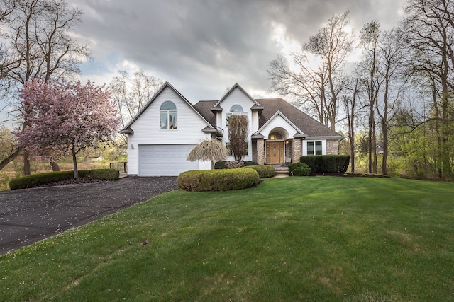 traditional-style home with a garage, a front yard, brick siding, and aphalt driveway