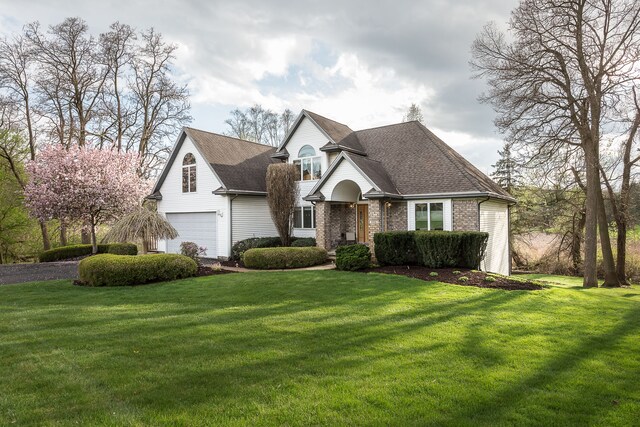 view of front of home featuring an attached garage, a shingled roof, a front lawn, and brick siding