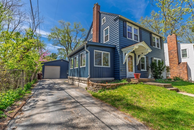 view of front of property featuring a chimney, a detached garage, fence, an outdoor structure, and aphalt driveway