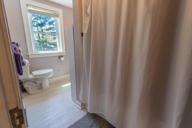 bathroom featuring toilet, baseboards, curtained shower, and wood finished floors