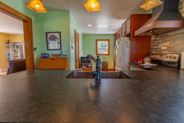 kitchen featuring freestanding refrigerator, wall chimney exhaust hood, a sink, backsplash, and stainless steel electric range oven