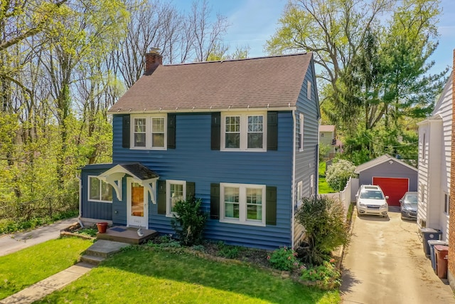 colonial home featuring a chimney, an outbuilding, a detached garage, a front lawn, and concrete driveway
