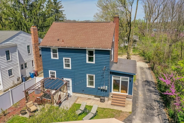 back of property with fence, a shingled roof, entry steps, a chimney, and a patio