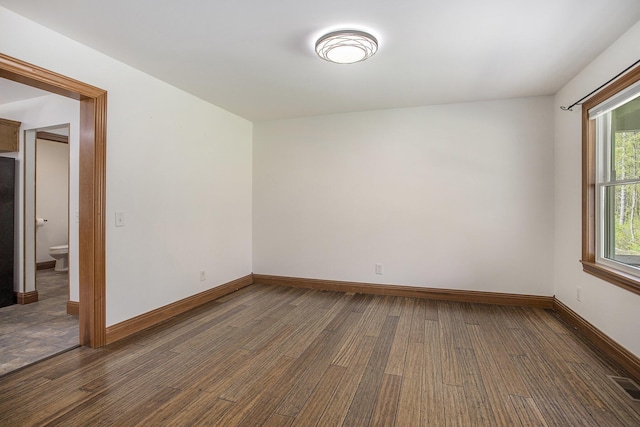 unfurnished room with baseboards, dark wood-style floors, and visible vents