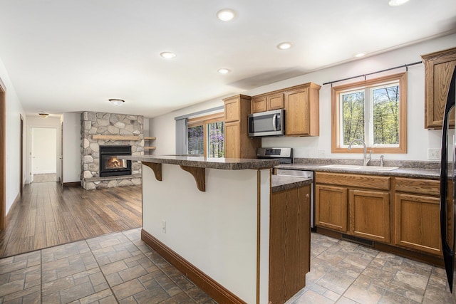 kitchen featuring dark countertops, a sink, a fireplace, stainless steel appliances, and a kitchen bar