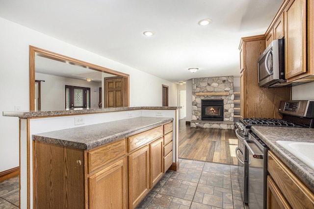kitchen with a fireplace, stainless steel appliances, open floor plan, stone finish flooring, and baseboards