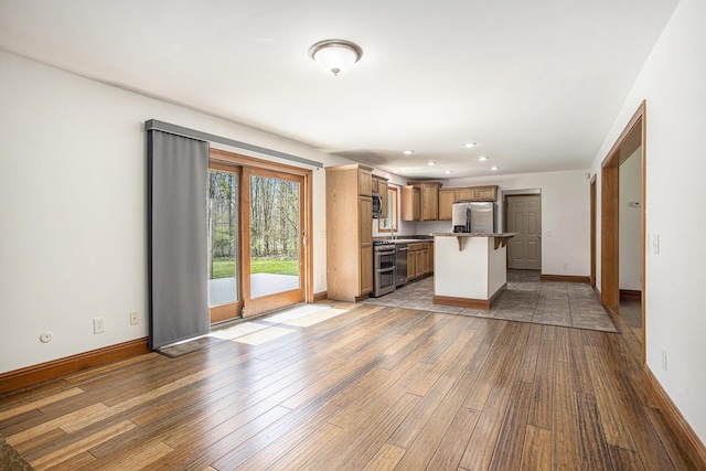 unfurnished living room with wood-type flooring, recessed lighting, baseboards, and a sink