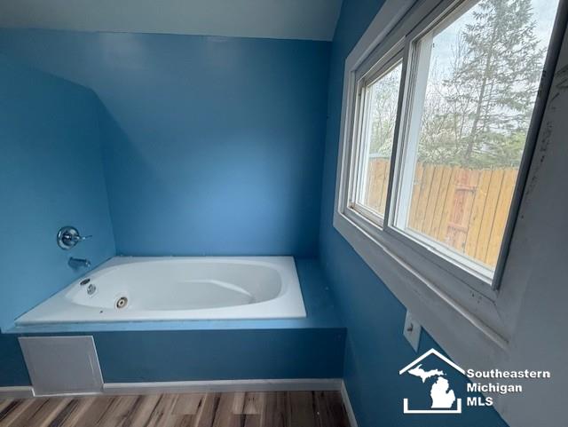 full bathroom featuring baseboards, wood finished floors, and a bath