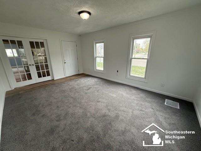 unfurnished room with a textured ceiling, french doors, carpet, baseboards, and visible vents
