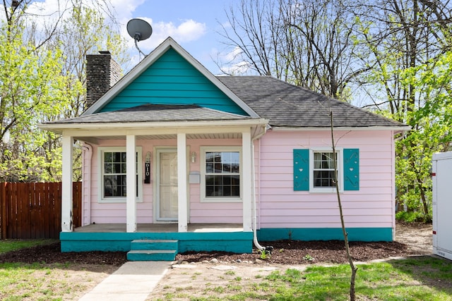 bungalow featuring a porch, fence, a chimney, and a shingled roof