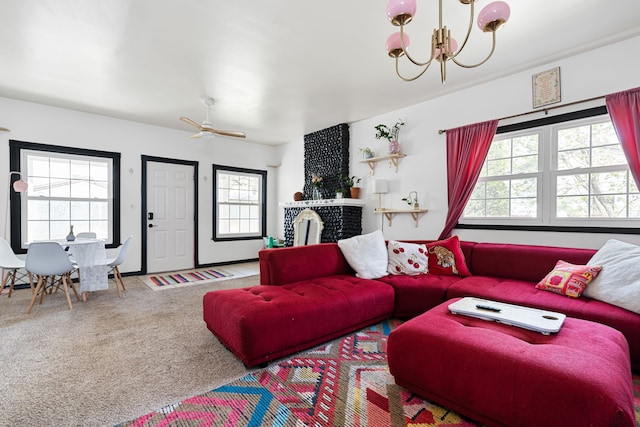 carpeted living area with ceiling fan with notable chandelier and a brick fireplace