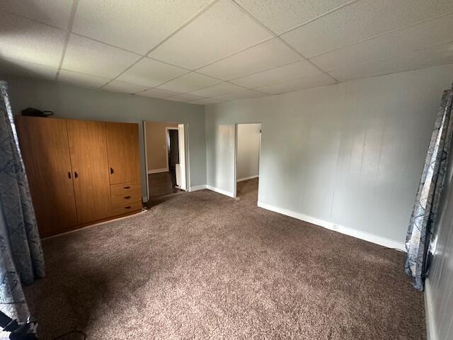unfurnished bedroom featuring dark colored carpet, baseboards, and a drop ceiling