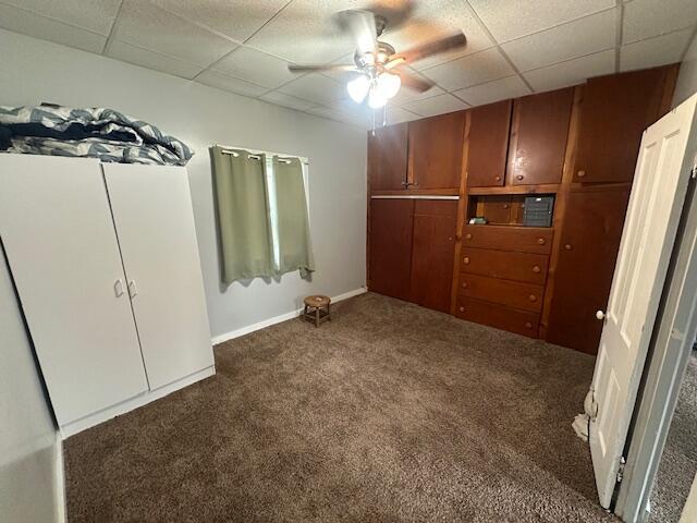 unfurnished bedroom with baseboards, carpet, a ceiling fan, and a paneled ceiling