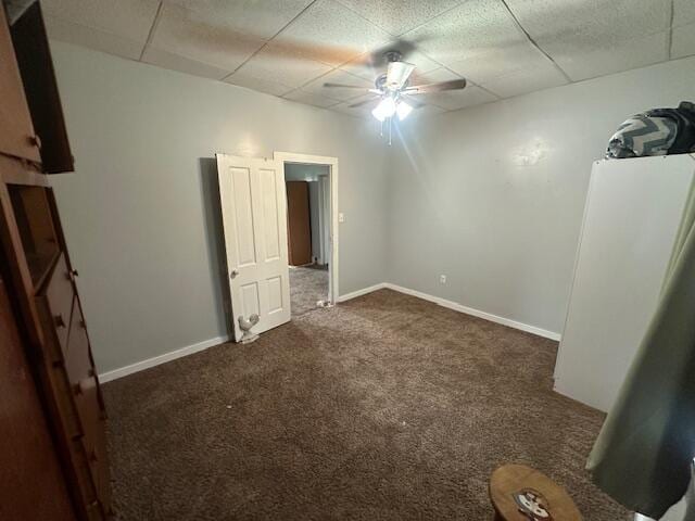 unfurnished bedroom with baseboards, ceiling fan, a drop ceiling, and dark colored carpet