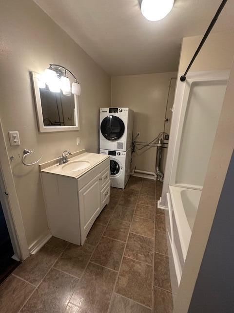 bathroom featuring vanity, baseboards, shower / bathtub combination, and stacked washer and dryer