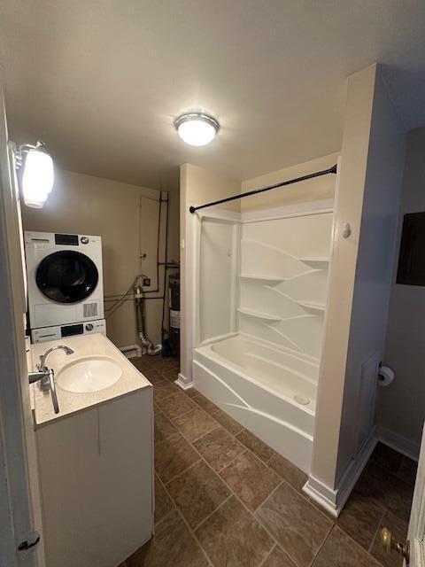 full bathroom featuring a shower, baseboards, vanity, and stacked washer / dryer