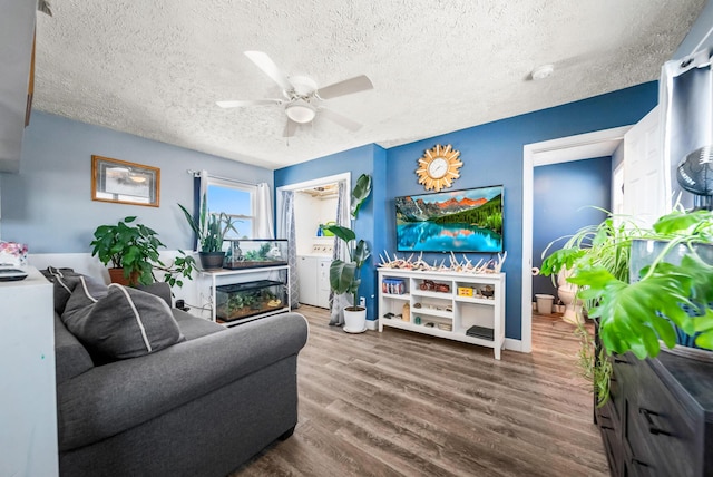 living area with ceiling fan, a textured ceiling, wood finished floors, baseboards, and washer and clothes dryer