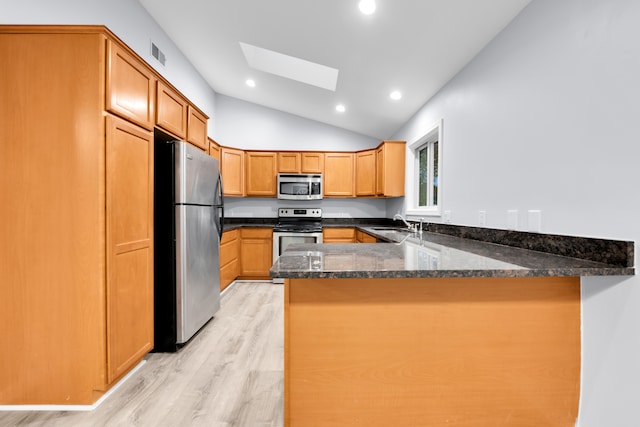 kitchen featuring appliances with stainless steel finishes, a sink, light wood finished floors, a peninsula, and lofted ceiling with skylight