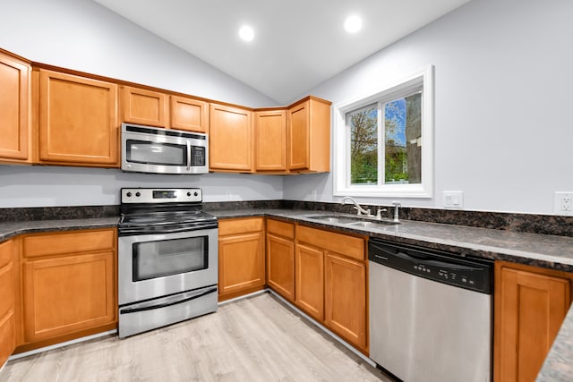 kitchen with a sink, dark stone countertops, lofted ceiling, light wood-style floors, and stainless steel appliances