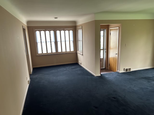 unfurnished room with baseboards, dark carpet, and visible vents