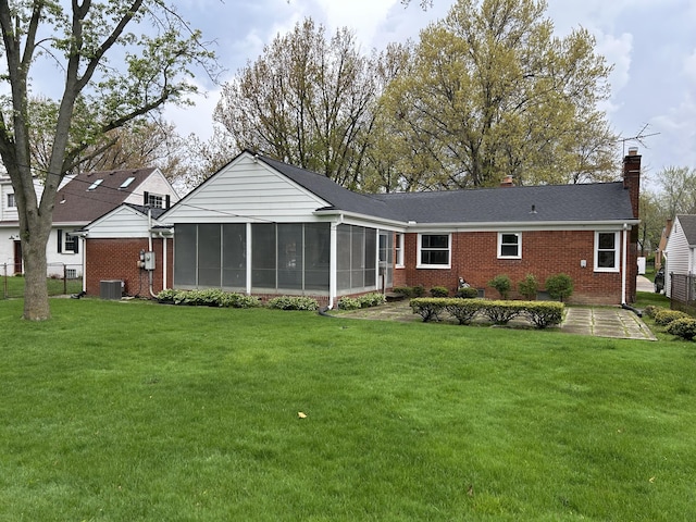 rear view of property with a lawn, brick siding, a chimney, and a sunroom