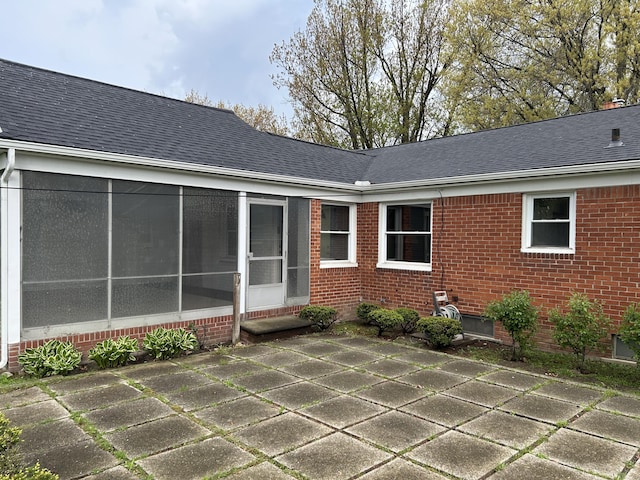 rear view of house featuring brick siding, roof with shingles, a patio area, and a sunroom