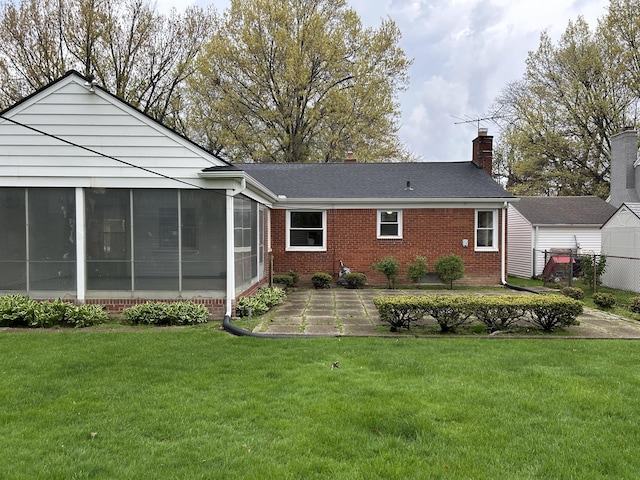 rear view of property with a chimney, brick siding, a sunroom, a patio area, and a lawn