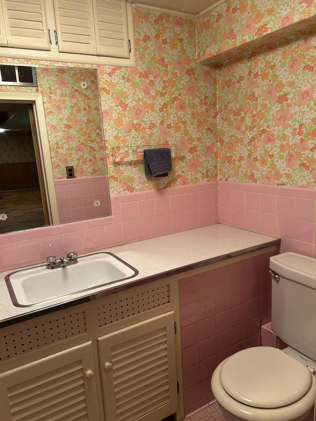 bathroom with vanity, toilet, a wainscoted wall, wallpapered walls, and tile walls