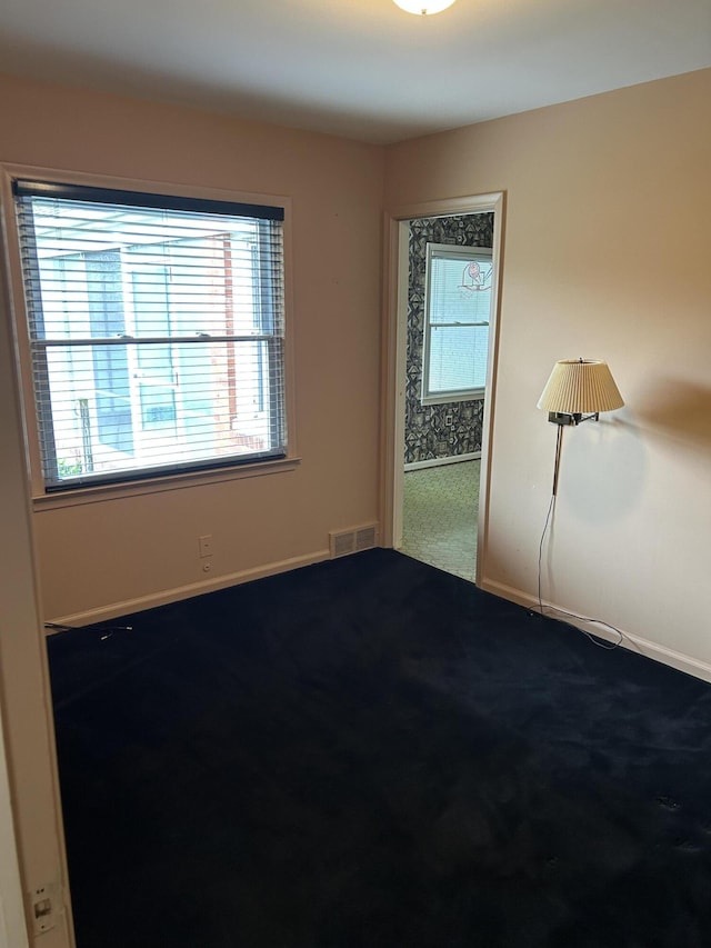 unfurnished room featuring visible vents, baseboards, and dark carpet
