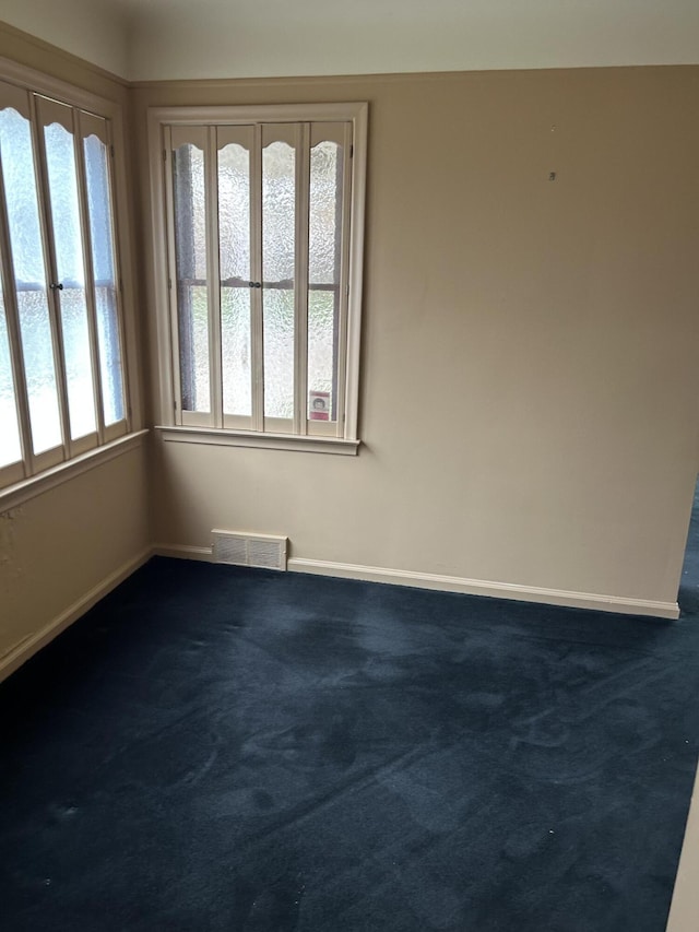 spare room featuring visible vents, baseboards, and dark carpet