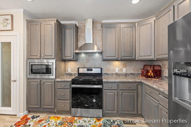 kitchen with wall chimney range hood, appliances with stainless steel finishes, tasteful backsplash, gray cabinetry, and ornamental molding
