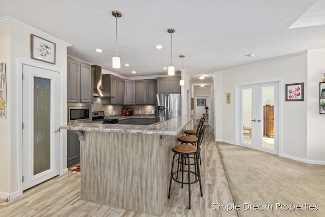 kitchen with a kitchen breakfast bar, backsplash, appliances with stainless steel finishes, ornamental molding, and wall chimney exhaust hood