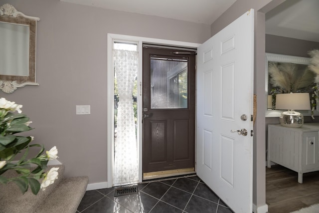 foyer featuring baseboards and dark tile patterned floors