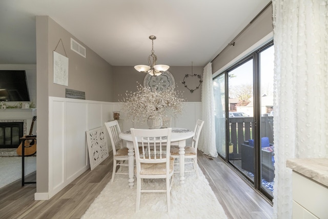 dining space featuring visible vents, a wainscoted wall, a glass covered fireplace, a chandelier, and light wood-style floors