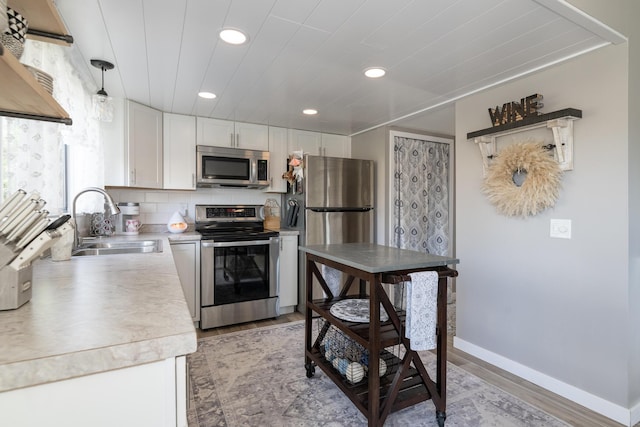 kitchen with a sink, light wood-style flooring, appliances with stainless steel finishes, and white cabinetry