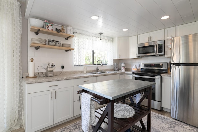 kitchen featuring white cabinets, a sink, stainless steel appliances, light wood-type flooring, and backsplash