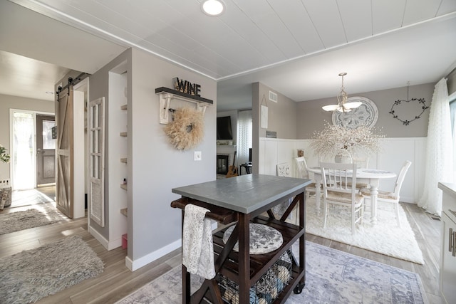 dining area with a barn door, a chandelier, baseboards, wood finished floors, and visible vents