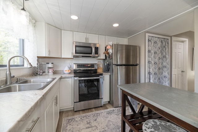 kitchen featuring appliances with stainless steel finishes, a sink, light countertops, white cabinets, and light wood-style floors