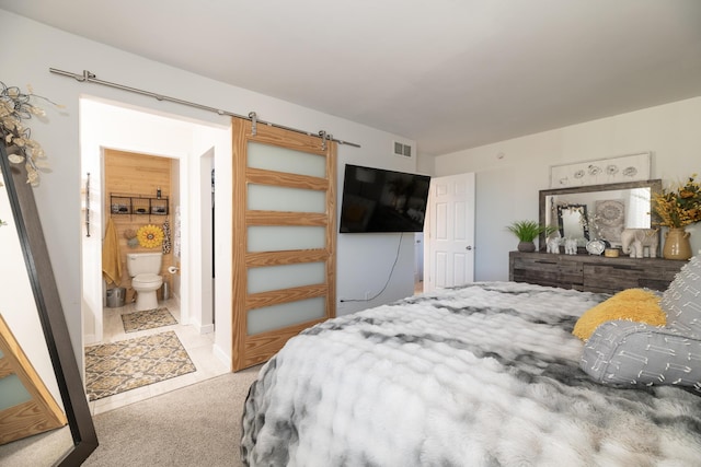 carpeted bedroom with visible vents, a barn door, and ensuite bath