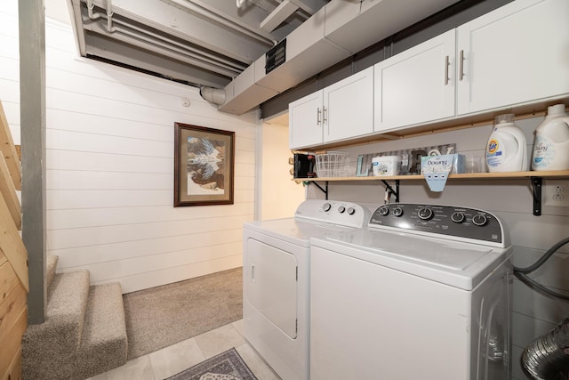 laundry room with cabinet space, wooden walls, light tile patterned flooring, light carpet, and washer and clothes dryer