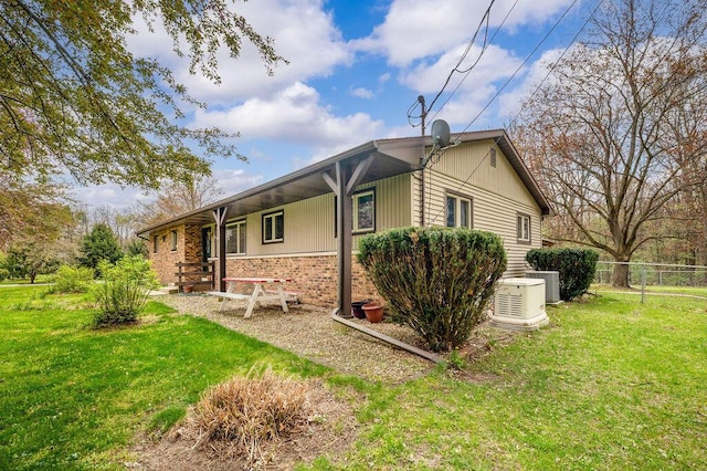 view of side of home featuring fence, cooling unit, a yard, and brick siding