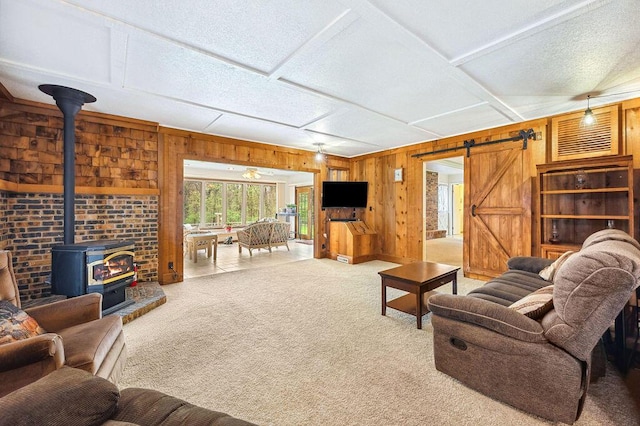 carpeted living room featuring a wood stove, wood walls, and a barn door