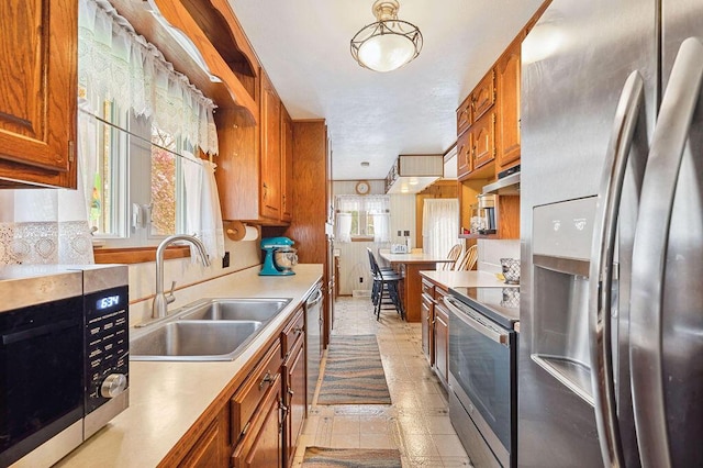 kitchen with brown cabinets, a sink, light countertops, under cabinet range hood, and stainless steel appliances