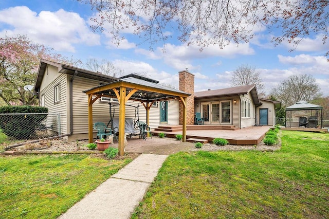 back of house featuring a chimney, a lawn, a wooden deck, a gazebo, and fence