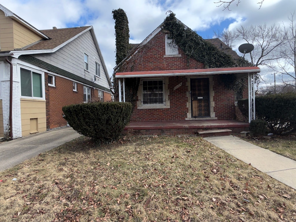 bungalow featuring a porch, a front lawn, and brick siding